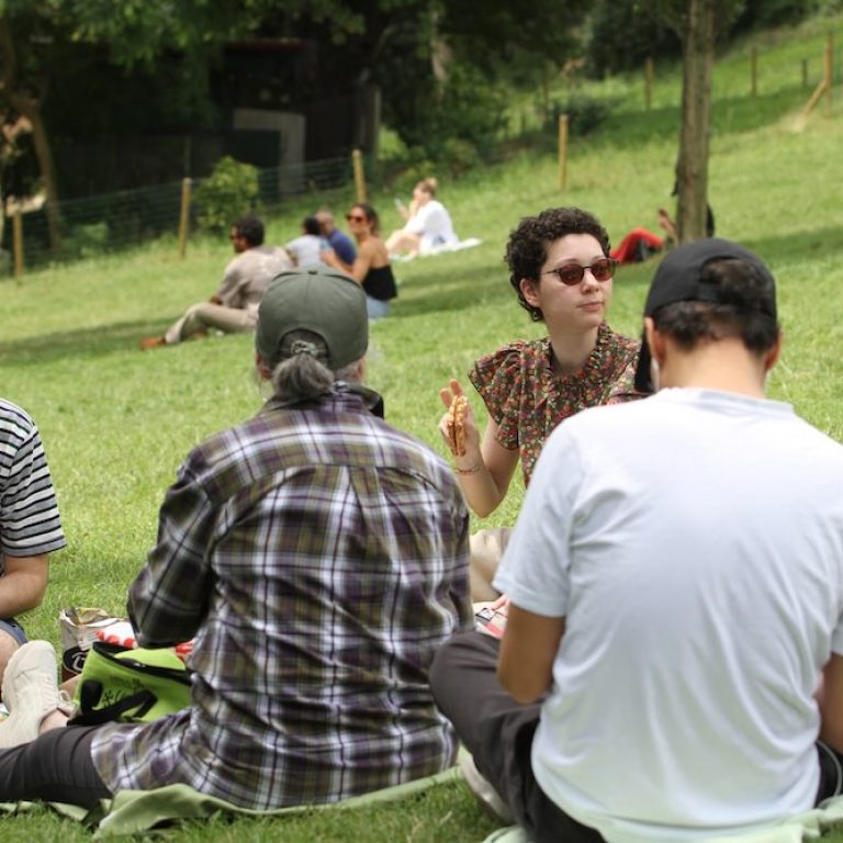 Membres du GEM TSA/TND de Paris réunis dans un parc pour un pique-nique, discutant et partageant un moment chaleureux en plein air, illustrant l’inclusion, la pair-aidance, l’autonomie et la vie sociale au sein du GEM.